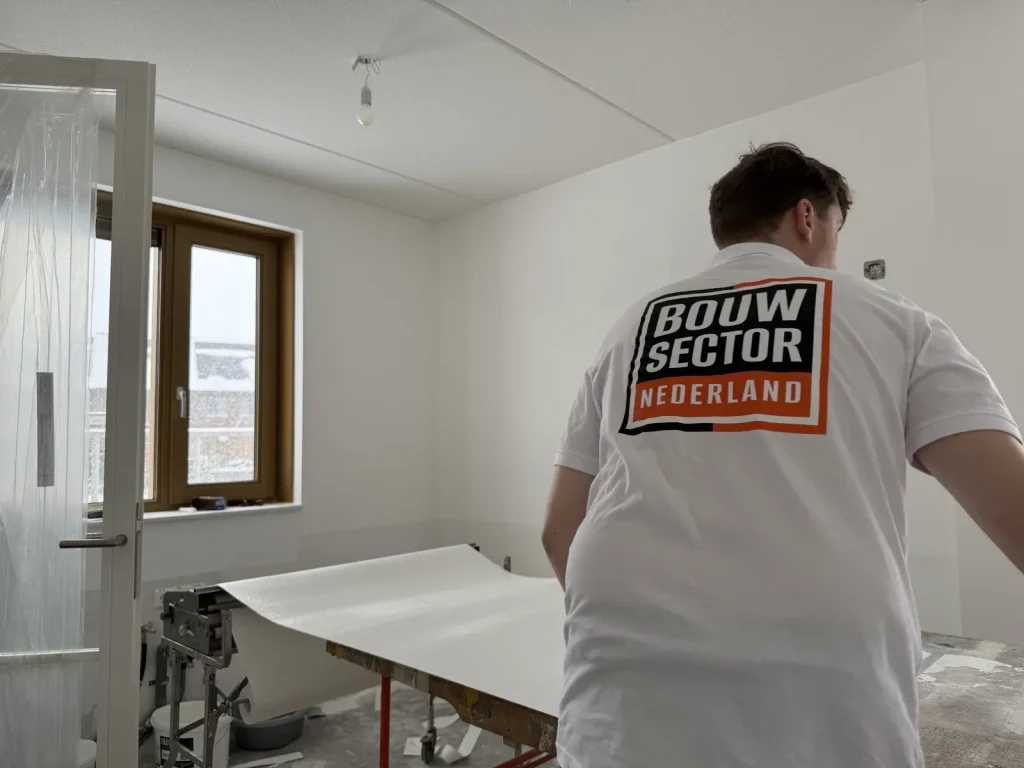 Vakman van Bouwsector Nederland bij de plaktafel met een baan vlies, deur afgeschermd met folie