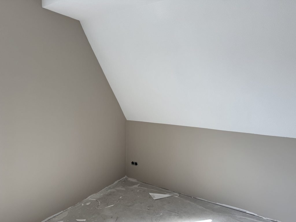 Zolderkamer met een schuine wand in wit en rechte wanden in een zachte grijsbeige tint, net afgewerkt