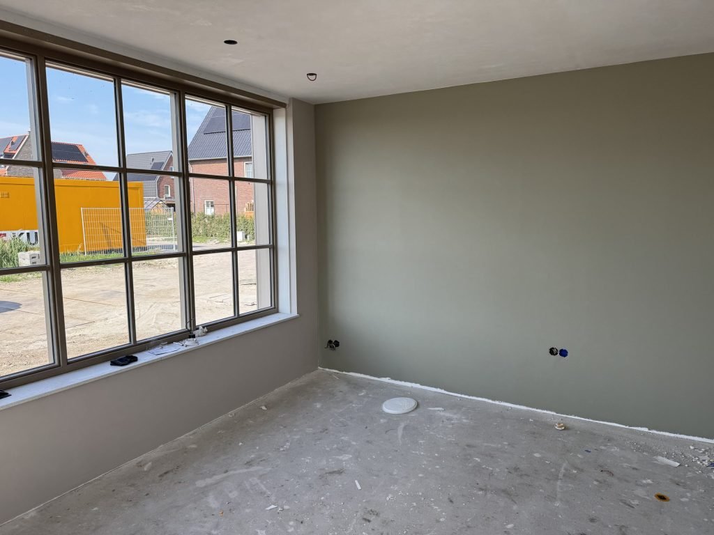 Kamer met een grijsgroen afgewerkte wand en een groot raam met kleine ruitjes