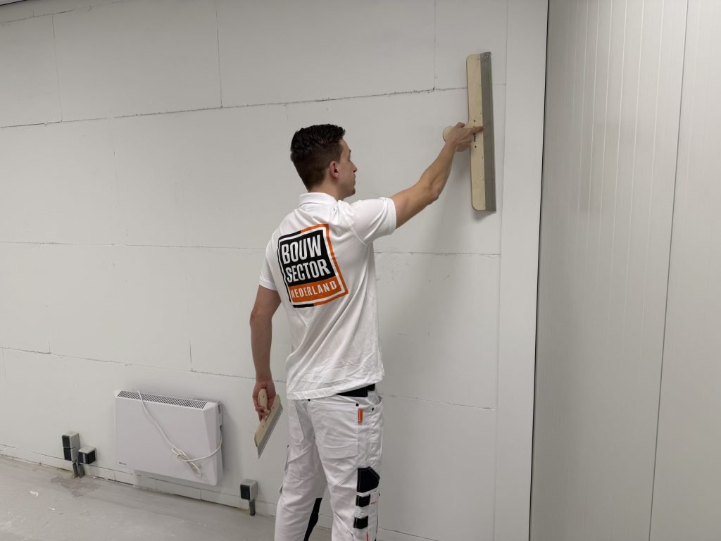 Stukadoor van Bouwsector Nederland zet een wand vlak met een lange spaan